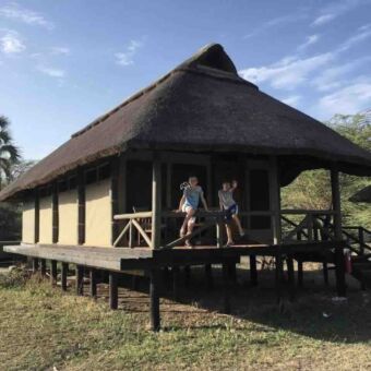 tented huisje met rietendak op palen met zwaaiende kinderen op de veranda accomodaties tanzania safari