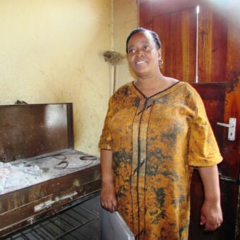 Tanzaniaanse vrouw met lange goud kleurig jurk bij een kooktoestel op hout cultuur activiteit tanzania