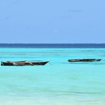 twee vissersbootjes in azuurblauwe zee bij Zanzibar strand