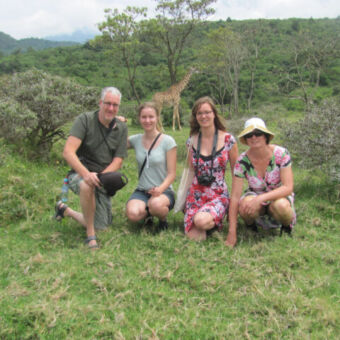 Familiefoto met een giraf op de achtergrond tijdens een wandel safari in Arusha National Park