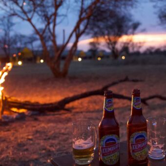 groot kampvuur links met op de voorgrond twee kilimanjaro biertjes op een tafeltje bij leen lodge in tanzania
