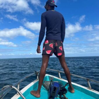 man staand op de blauwe romp van een houten boot uitkijkend over het Tanganikya meer in Tanzania