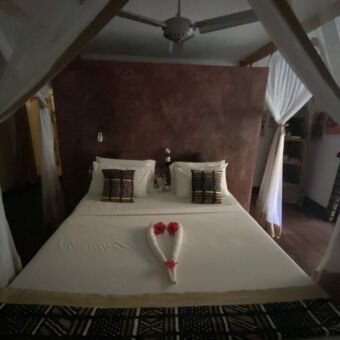 groot bed met witte lakens en handdoeken gevouwen in de vorm van een hartje erop