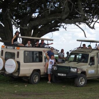 tien mensen die voor de auto's staan van droomreis tanzania gedurende een safari rondreis