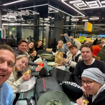 gasten van droomreis tanzania die voor vertek op schiphol met z'n tienen aan een tafel zitten te ontbijten