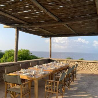 grote tafel met stoelen onder een veranda bij manayara secrets met daarachter lake manyara bij