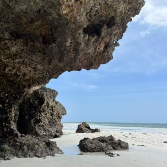 Prachtige witte ruige stranden op Zanzibar Safari Tanzania reizen ter inspiratie. Op Zanzibar vanaf het witte strand is een grote rots met daarachter de azuur blauwe wateren van de Indische oceaan.