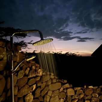 buitendouche bij lahia tented camp op de serengeti. de douche is ommuurt uit losse stenen en je hebt uitzicht over de serengeti