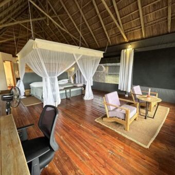 overzicht van een grote luxe kamer bij lahia tented kamp. er staat een groot bed met klamboe op de achtergrond en op de voorgrond twee luie stoelen die uitkijken over de serengeti