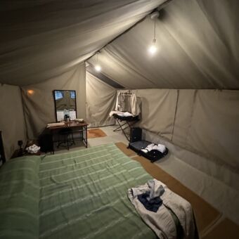 binnen in een safari tent van kati kati zie je een groot twee persoons bed met groene lakens