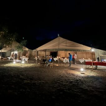 safaritent die gebruikt wordt als dining area voor de gasten. er staan veel tafels klaar voor het diner en er lopen een aantal mensen rond