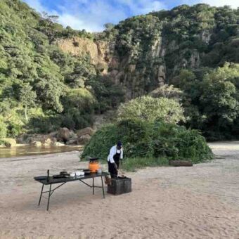 op de zandoever van een rivier in lake manyara bij het green camp een kok die op een tafel het eten is aan het voorbereiden