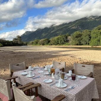 op een rivierbedding in lake manyara een mooi gedekte tafel met stoelen erom voor de lunch
