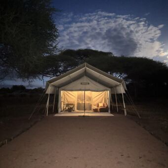 grote safari tent van voren met de lichten binnen aan en twee stoelen ervoor