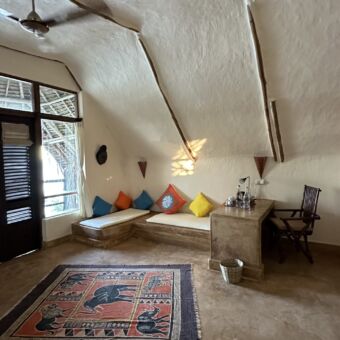 overzicht van een kamer bij sunshine marine lodge. Er is een rechthoekige bank met kussens en kleurige kussens de muren kalk wit en kleine houten balken