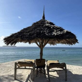 rieten ronde parasol met daaronder twee ligbedden op het parelwitte strand van zanzibar met uitzicht op de indische oceaan