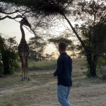 man die op de grond staat kijkend naar een giraf op de serengeti