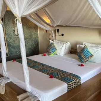 Groot mooi opgemaakt bed met witte lakens en kleurige kussens met erom heen een houten fram waar een klamboe aanhangt bij sushine marine lodge