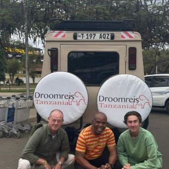 reizigers van droomreis Tanzania poserend door de hurken achter de safari auto van droomreis Tanzania