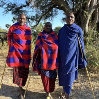 drie Masai Manne poseren. ze hebben alle drie hun stok en zijn gekleed in oranje en blauw gekleurde gewaden
