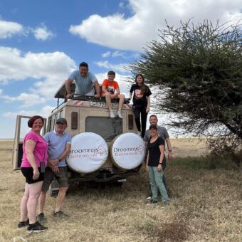 Familie safari rondreis. Met opa de kinderen en ouders die op safari zijn. Ze staan in, op en achter de auto van Droomreis Tanzania