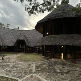 overzicht foto van een lodge in Selous. op de voorgrond plaveisel en daarachter de lodge die opgetrokken is uit hout en een rieten dak