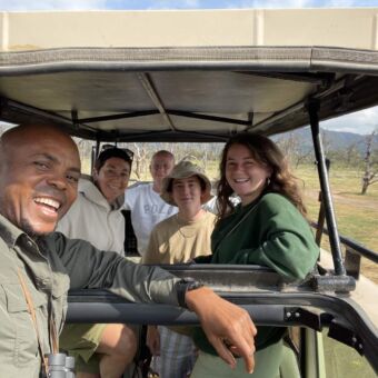 Selfie van gasten van Droomreis Tanzania samen hun gids in Tarangire National Park Reiservaring Safari Tanzania. Een selfie van een gids met reizigers van Droomreis Tanzania tijdens hun rondreis door Tanzania. Ze staan in de safari auto met het dak omhoog midden in Tarangire National Park