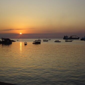 zonsondergang bij de indische oceaan van zanzibar. er liggen mooie houten bootjes die dobberen op het kalme water