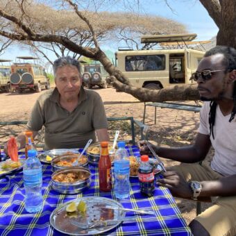 Safari Tanzania. Een man en zijn gids zitten aan tafel op een picknickplek met een hoflunch in Tarangire National Park
