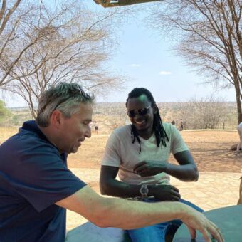 Tanzania safari. Man met zijn gids zitten aan een tafel en praten en lachen