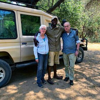 Reiservaring Rondreis Tanzania. Twee gasten van Droomreis Tanzania met hun gids staan naast hun safariauto in Karatu