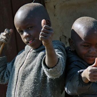 Twee kindertjes in smoezelige kleding met de duimen omhoog. Tijdens een bezoek aan Masai Boma. Reisverhalen Tanzania
