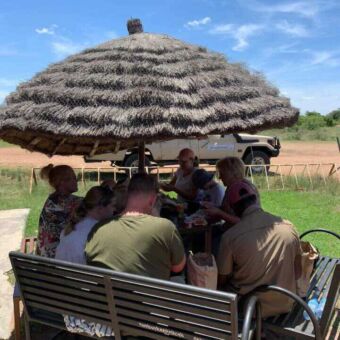 Lunchen op een picknickplek in Tarangire Tanzania. Gasten zitten samen onder een rietenparasol te lunchen
