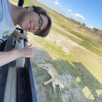 Tijdens een rondreis door Tanzania staat de safariauto naast een slapende leeuwin en een jongen staat in de auto en hangt iets voorover. Hierdoor staat hij samen met de leeuwin op de foto