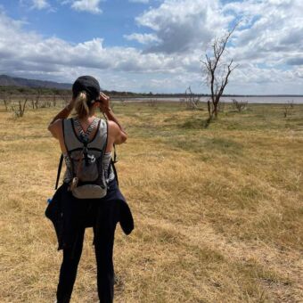 Safari tanzania. Tijdens een wandelsafari kijkt een vrouw met de verrekijker over de goudgele vlaktes met daarachter een meer of ze iets kan spotten