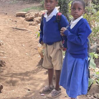 Onderweg tijdens een rondreis door Tanzania komen reizigers twee meisjes tegen die in hun blauwe schooluniformen onderweg zijn naar school