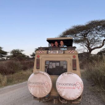 Tanzania safari. Safariauto van Droomreis Tanzania in Ndutu vlakbij de Serengeti. Drie gasten staan in de auto waarvan het dak omhoog is.