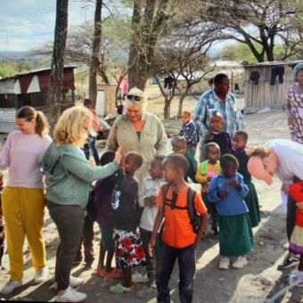 Culturele activiteit rondreis Tanzania. Gasten en lokale kinderen maken plezier en praten met elkaar tijdens een terug naar Tanzania reis