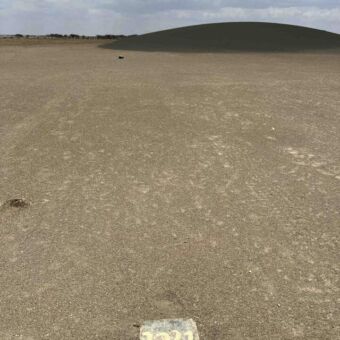 Shifting Sands Serengeti Tanzania. Een paaltje met het jaar 2021 erop. Daarachter waar de heuvel nu is. De heuvel verplaatst zich door de wind elk jaar een stuk van 25 meter.