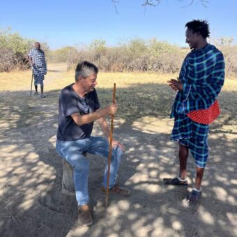 Man zit op een boomstronk en praat met een Masai Tanzania