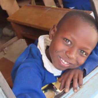 jongetje die je lachend aankijkt vanaf de schoolbank hangend uit het raam