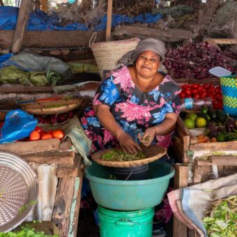 Tanzaniaanse vrouw zittend tussen al haar spullen op een markt