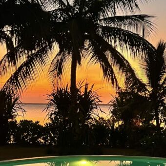 Zonsondergang met op de voorgrond een zwembad en daarachter een palm en de Indische oceaan
