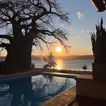 Zwembad met daarnaast een baobab en erachter Lake Manyara tijdens een zonsondergang