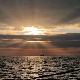 zonnestralen door de bewolking en in de verte een dhow op zee