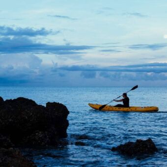 Kayakkende man op de Indische Oceaan met rotsblokken op de voorgrond en een mooie wolkenlucht erachter