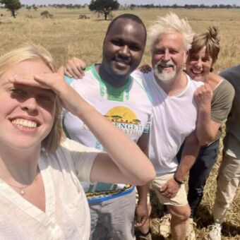 Een selfie van een lachende gids en vier familieleden in een open savannelandschap in Tanzania.