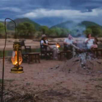 Olielampen met daarachter mensen die bij een kampvuur zittenin Ruaha National Park