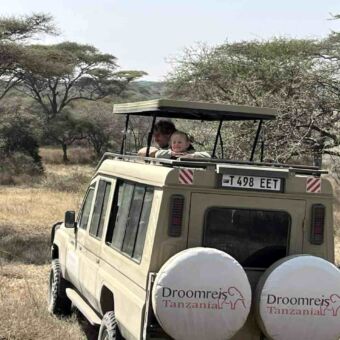Safari-auto met het dak omhoog met een meisje en een man die dieren aan het spotten zijn