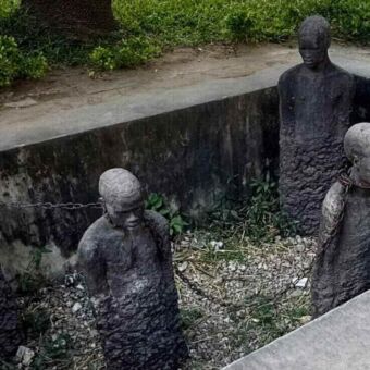 Het slavernijmonument in Stone Town, Zanzibar, met stenen beelden van tot slaaf gemaakte mensen die met kettingen om hun nek in een kuil staan.